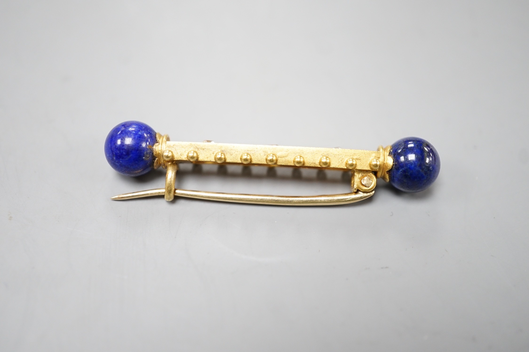 A yellow metal and three stone diamond set bar brooch. with lapis lazuli bead set terminals, 43mm, gross weight 4.8 grams.